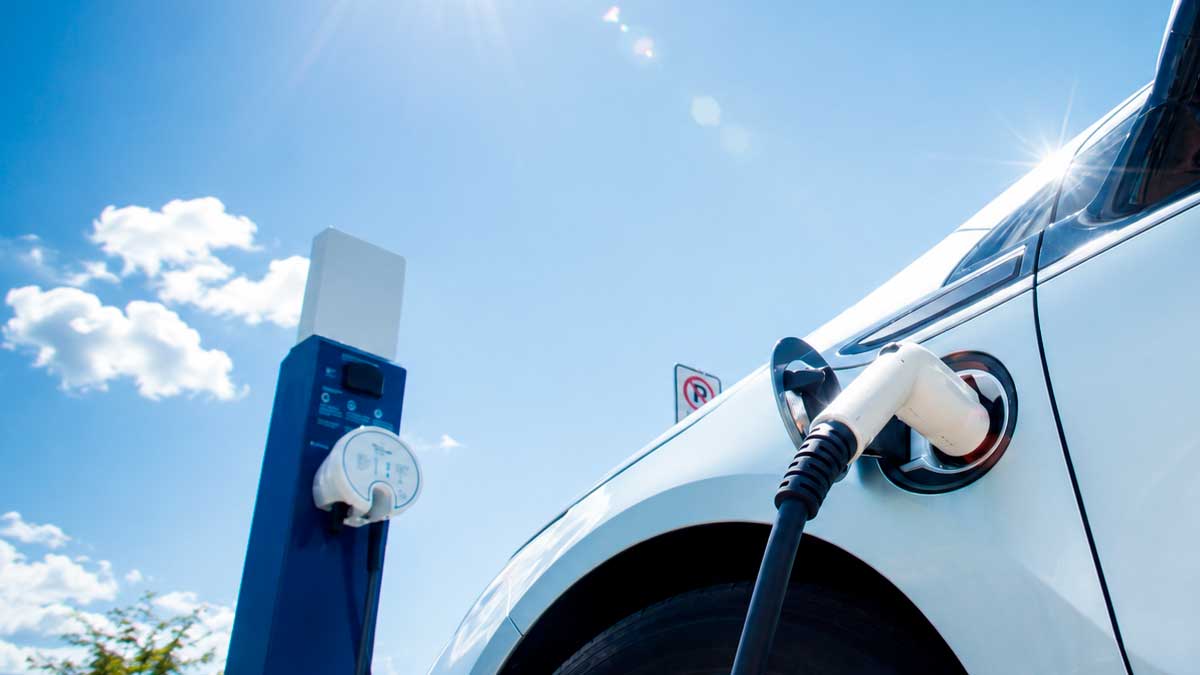 Coche eléctrico blanco cargando su batería en un punto de recarga bajo un cielo despejado.