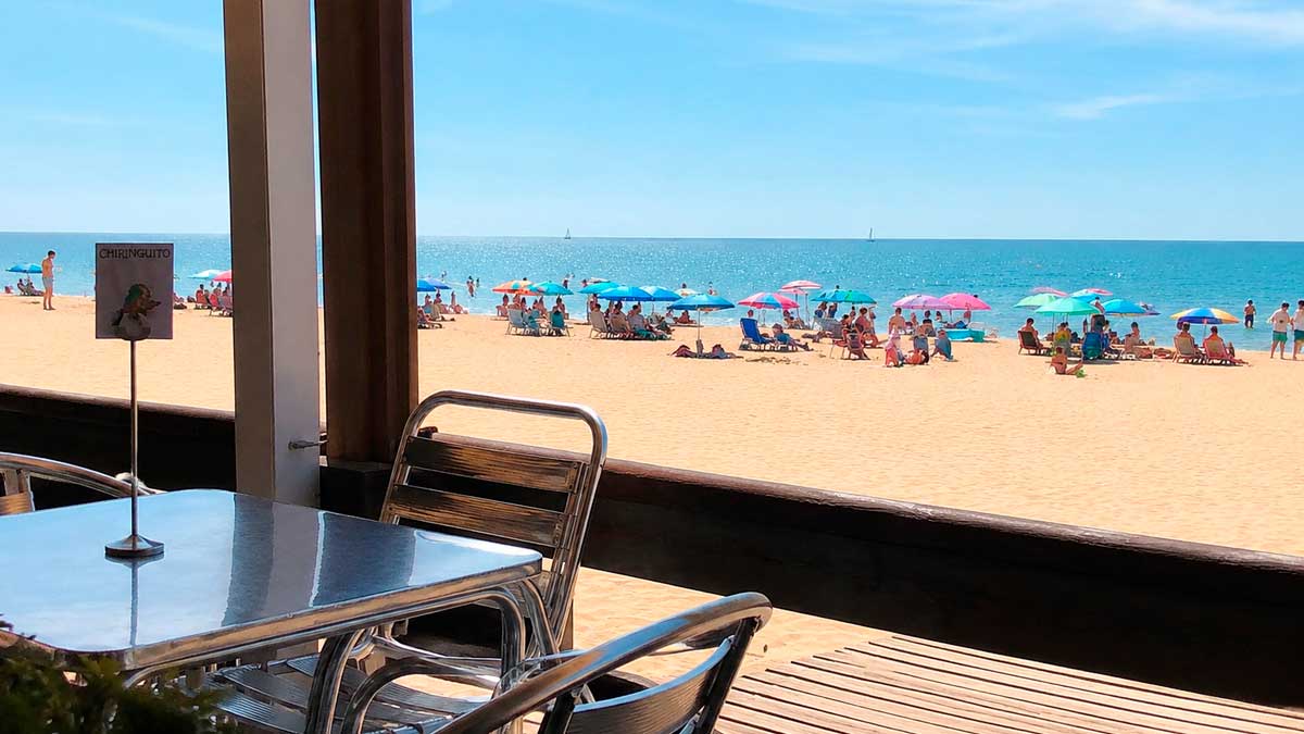 Terraza de un chiringuito con vistas a una playa concurrida en la costa de Andalucía.