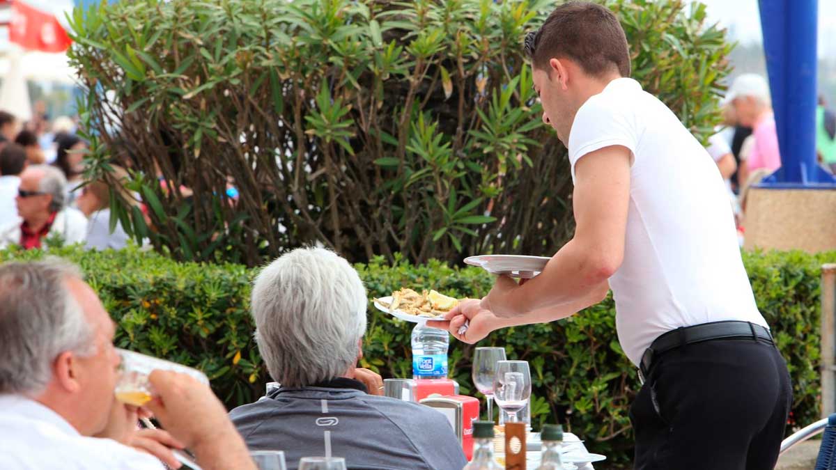 Camarero atendiendo a clientes en terraza de restaurante, empleo turístico en Andalucía