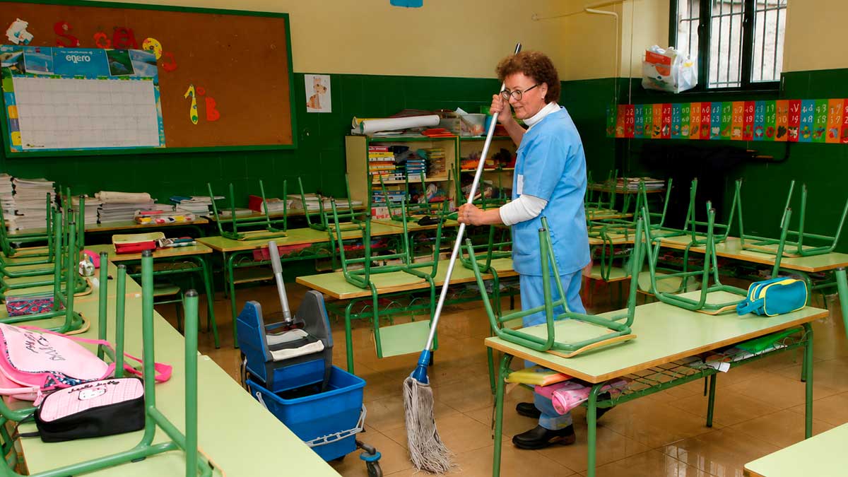 Trabajadora de limpieza en colegio de Sevilla limpiando un aula con sillas sobre las mesas