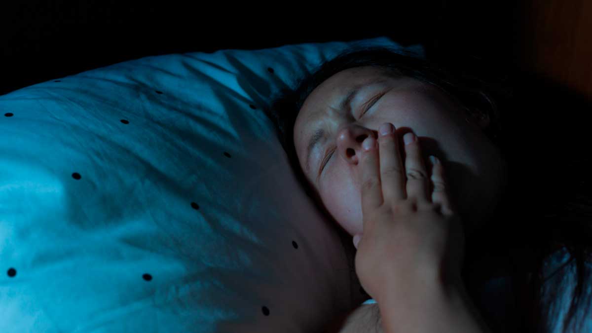 Persona bostezando en la cama, dormir a oscuras reduce el insomnio en Andalucía