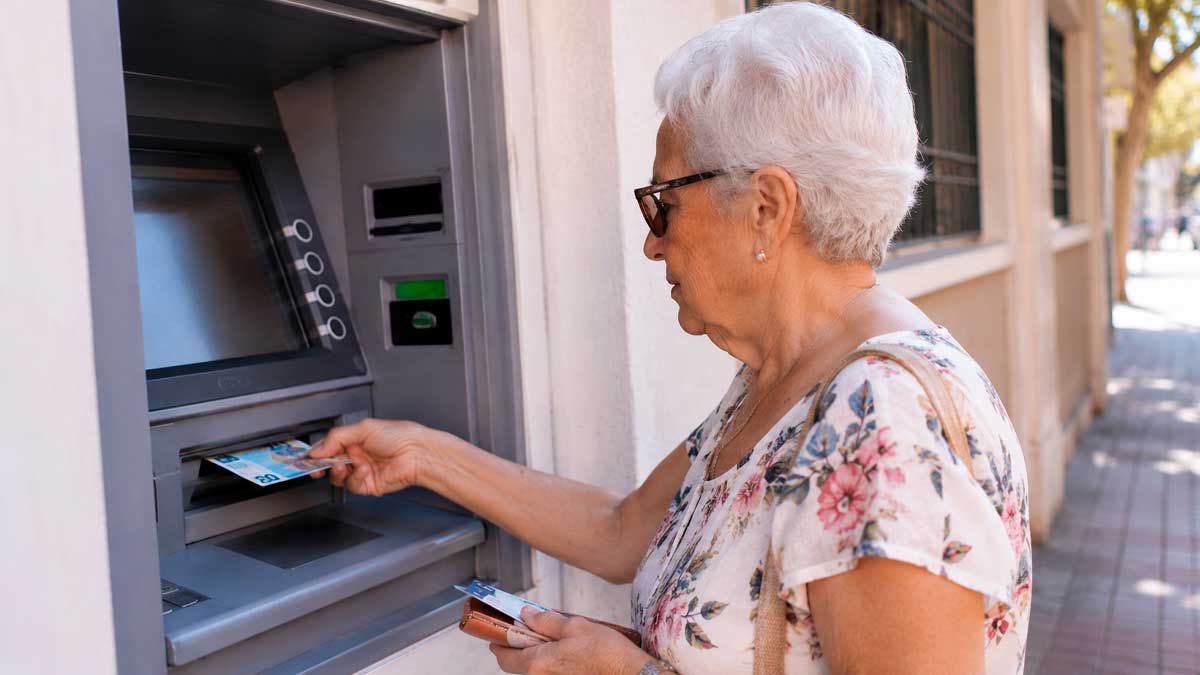 Mujer mayor retirando dinero de un cajero automático, pago de las pensiones en agosto de 2026