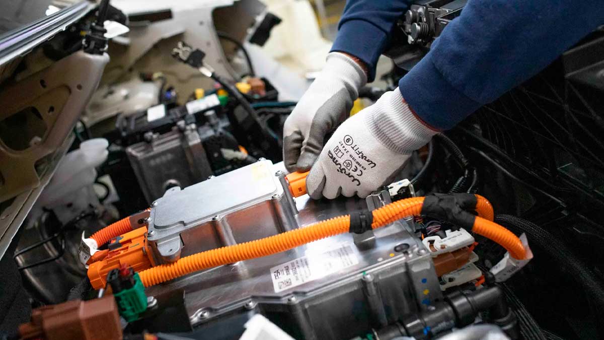 Mecánico en taller de coches eléctricos manipulando cables de alta tensión