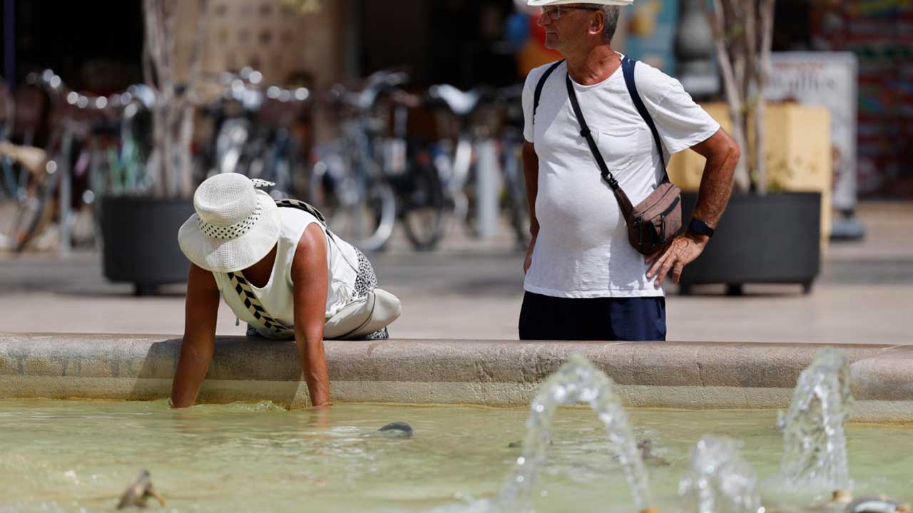 Dos personas se refrescan en una fuente durante una jornada de calor
