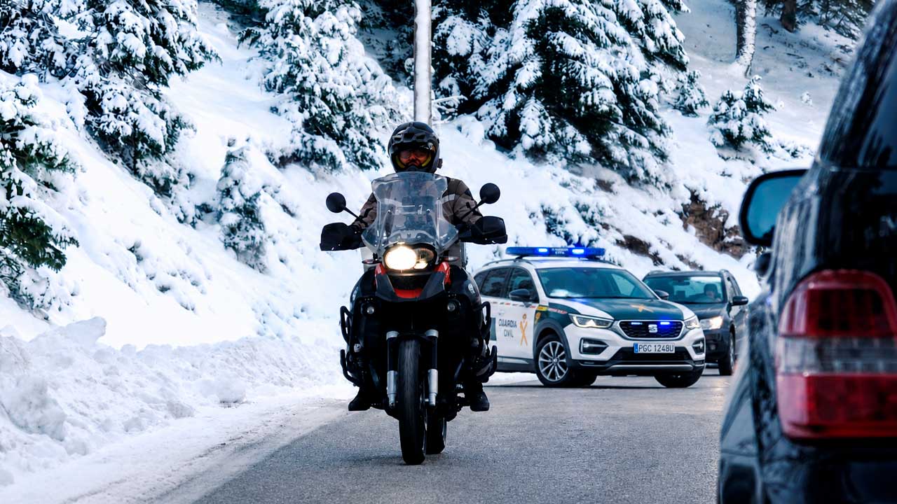 Motorista circulando por una carretera con nieve junto a un vehículo de la Guardia Civil