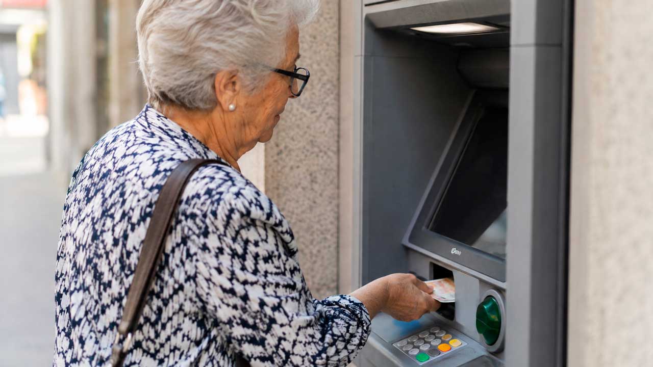 Pensionista saca dinero de su pensión de septiembre de 2026 de un cajero automático.