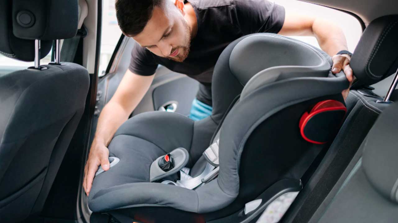 Adulto revisando una sillita infantil en el asiento trasero de un coche antes de la vuelta al cole