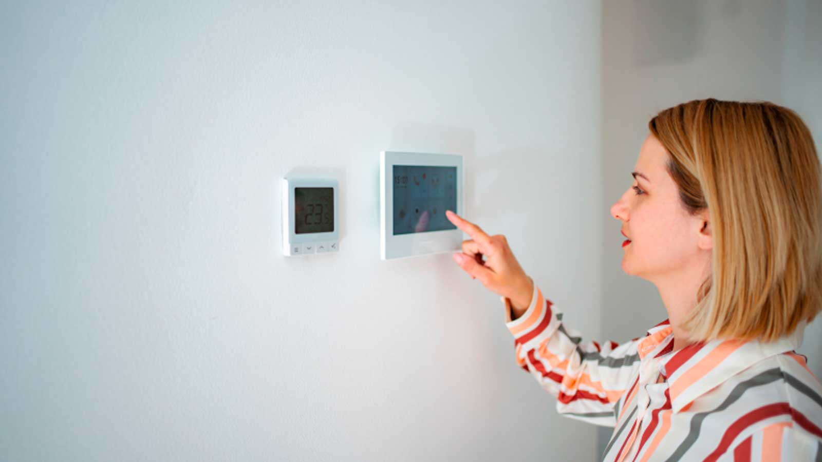 Mujer ajustando un termostato digital de calefacción en su vivienda antes del cambio de hora de octubre.