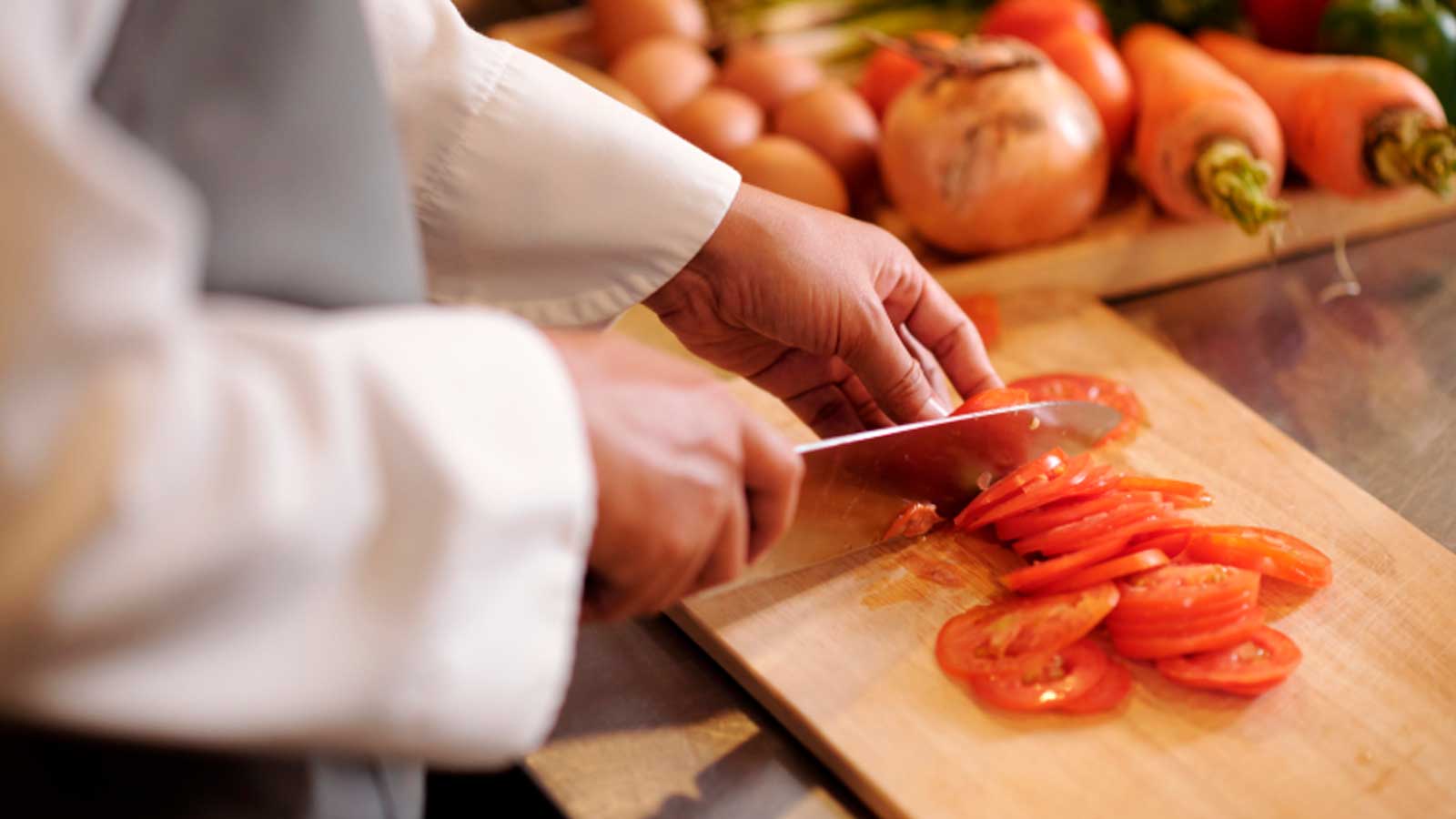 Cocinero cortando tomates con un cuchillo en una cocina profesional.