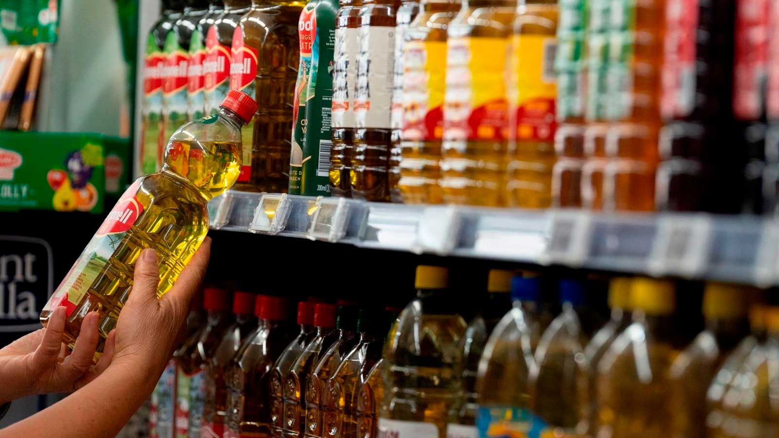 Persona revisando la etiqueta de una botella de aceite de oliva en un supermercado antes de comprarla.