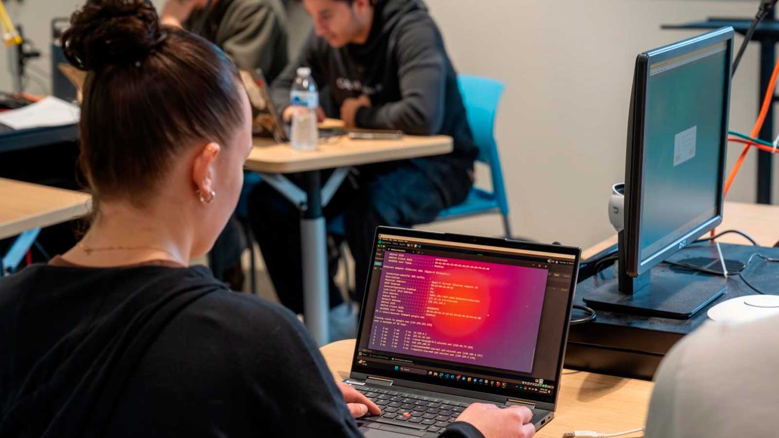 Alumna utilizando un ordenador portátil durante una clase de formación en ciberseguridad.