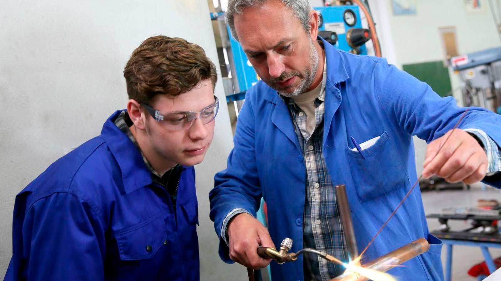 Trabajador experimentado enseña un oficio a un aprendiz en un taller industrial.