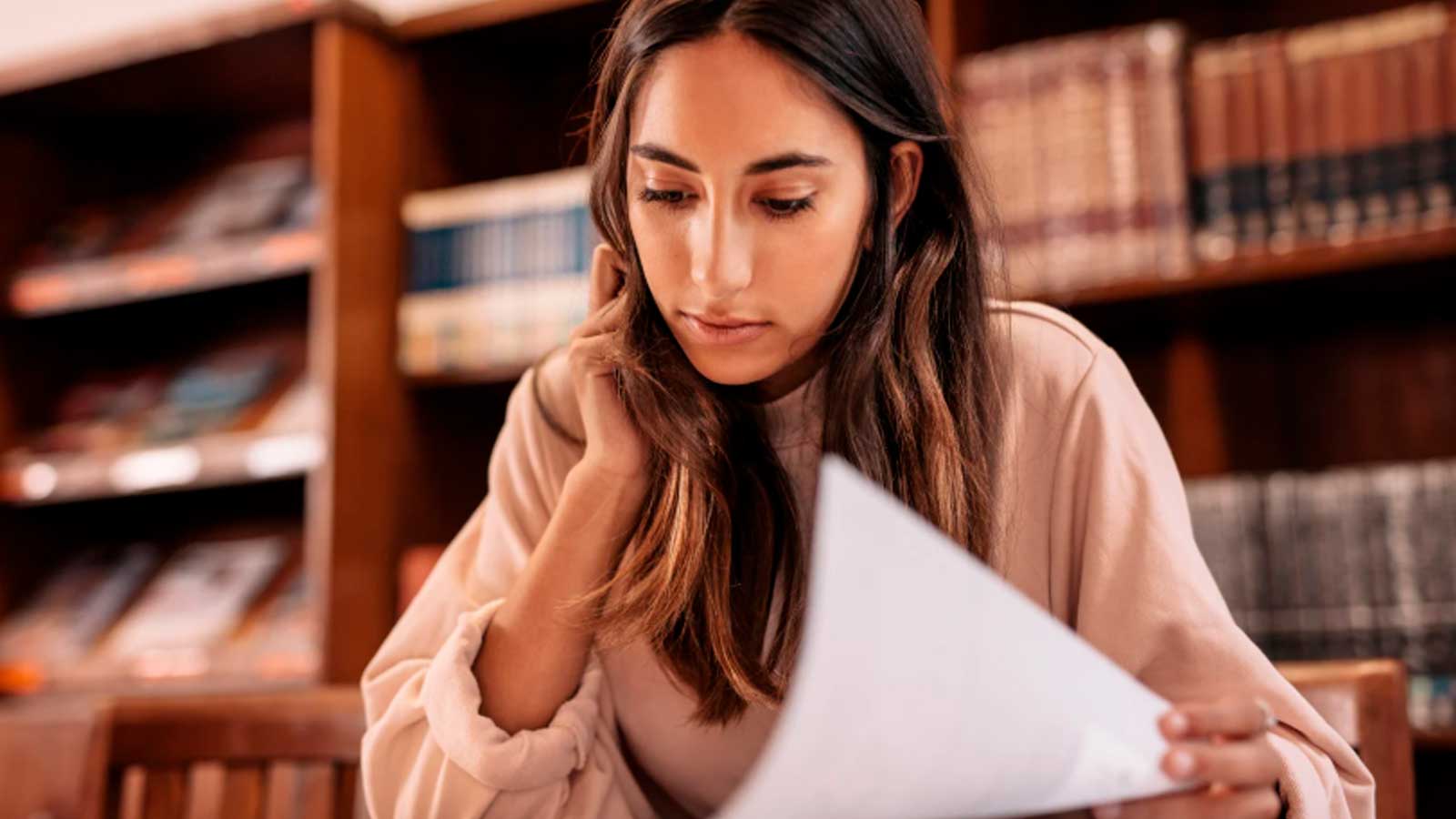 Joven estudiante consultando documentos en una biblioteca universitaria de Andalucía.