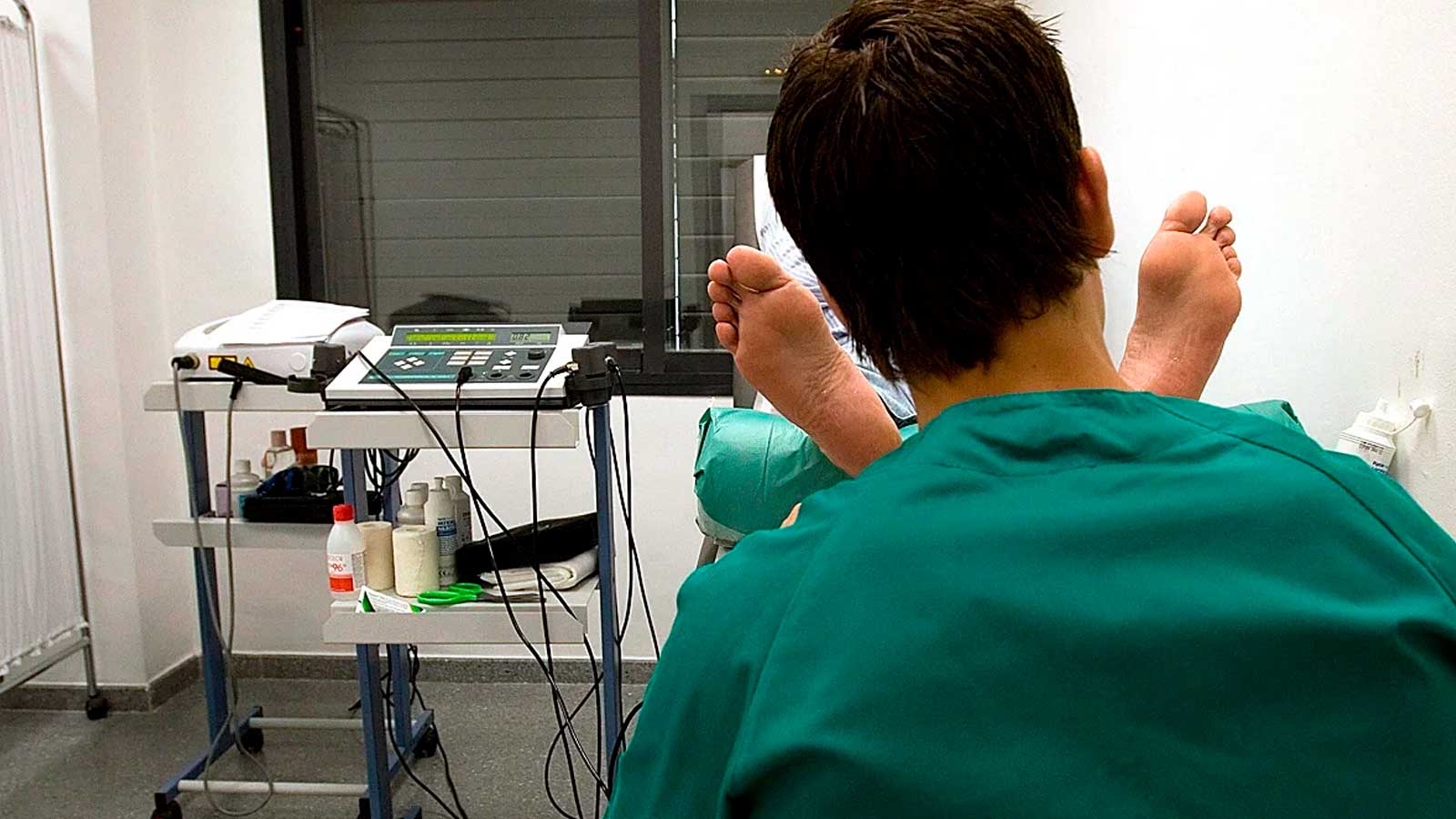 Podólogo atendiendo a un paciente en una consulta de podología con equipamiento sanitario.