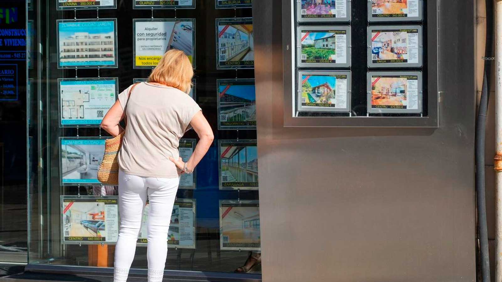 Mujer consulta viviendas en alquiler en el escaparate de una inmobiliaria